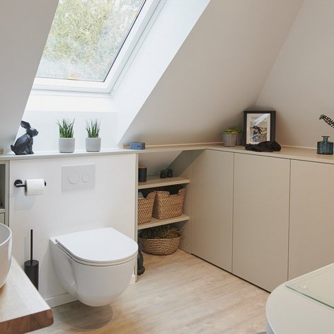 Ein modernes Badezimmer mit schrägen Wänden, einem großen Waschbecken und stilvollen Pflanzen auf der Fensterbank.