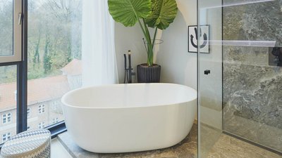 Ein modernes Badezimmer mit einer freistehenden Badewanne, großen Fenstern und Blick auf die Natur im Hintergrund.