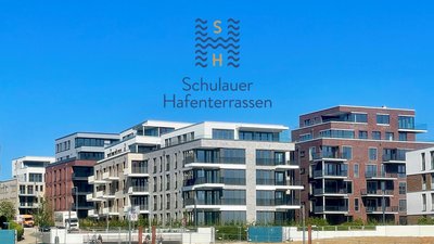 Moderne Wohngebäude mit großen Fenstern und Balkonen, die am Wasser stehen, unter einem strahlend blauen Himmel.