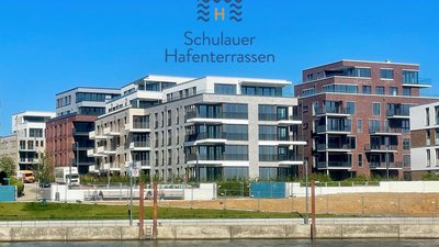 Moderne Wohngebäude mit großen Fenstern und Balkonen, die am Wasser stehen, unter einem strahlend blauen Himmel.
