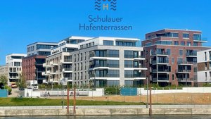 Moderne Wohngebäude mit großen Fenstern und Balkonen, die am Wasser stehen, unter einem strahlend blauen Himmel.
