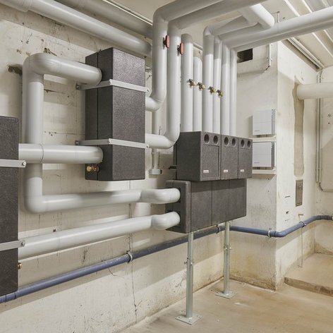 Die Wand ist mit verschiedenen Rohren und zwei großen schwarzen Geräten ausgestattet, die Teil eines Heizsystems sind.
