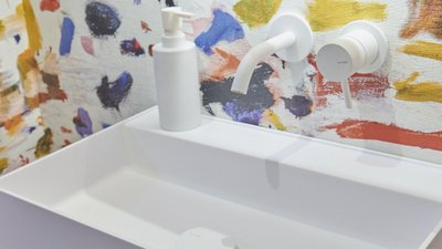 Ein modernes Waschbecken mit einem minimalistischen Design, umgeben von einer bunten, künstlerischen Wandgestaltung.