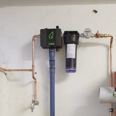 An einer Wand installierte Wasserleitungen und ein Filtergerät zeigen die technische Ausstattung eines Haushalts oder einer Industrieanlage.