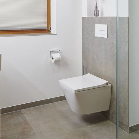 Das Badezimmer zeigt eine helle, minimalistische Gestaltung mit einem weißen Waschbecken und einer schlichten Toilette an der Wand.