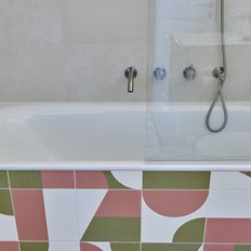Eine moderne Badewanne mit einer klaren Glasabtrennung und bunten Fliesen im unteren Bereich, die geometrische Muster zeigen.