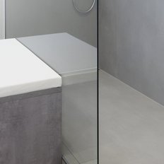 Der Raum kombiniert Funktionalität und Design, mit einem hellen Sitzbereich und einer modernen, klaren Duschabtrennung.