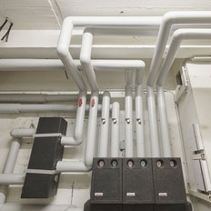 Ein komplexes Rohrsystem aus weißen Rohren, das an einer Wand montiert ist, mit verschiedenen Ventilen und Messgeräten.
