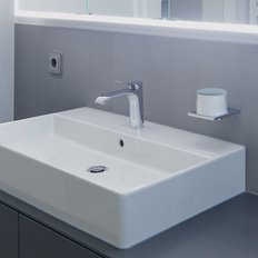 Das Waschbecken ist mit einem modernen Wasserhahn ausgestattet, während die Wände in neutralen Grautönen gehalten sind.