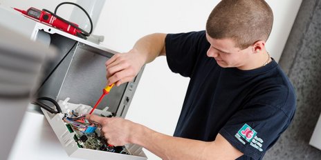 Ein Techniker arbeitet konzentriert an einem offenen Gehäuse, während er mit einem Schraubendreher Kabel verbindet.