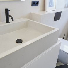 Das Waschbecken aus hellem Beton steht neben einer weißen Toilette, umgeben von stilvollen Fliesen in Schwarz und Weiß.