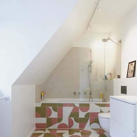 Ein modernes Badezimmer mit schrägen Wänden, einer Badewanne und bunten, geometrischen Fliesen auf dem Boden.