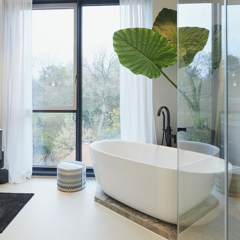 Ein modernes Badezimmer mit einer freistehenden Badewanne, großen Fenstern und einem Blick auf die Natur im Hintergrund.