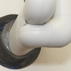 Ein graues Rohr mit einem gebogenen Ende ist in eine Wandöffnung integriert, die einen industriellen Look vermittelt.
