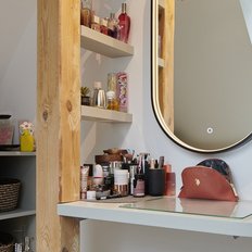 Der Schminktisch zeigt eine Vielzahl von Parfums und Kosmetikartikeln, ergänzt durch eine moderne Lampe und eine dekorative Ablage.