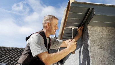 Ein Dachdecker der an einem Dach arbeitet und einen Hammer in der Hand hat
