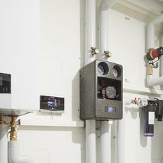 Eine moderne Heizungsanlage mit digitalen Anzeigen und Rohren, die an einer weißen Wand installiert sind.
