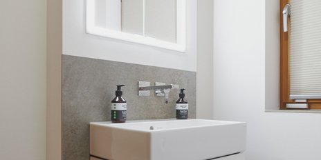 Ein modernes Badezimmer mit einem weißen Waschbecken und zwei Seifenspendern auf einer grauen Wandverkleidung.