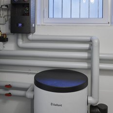 In einem Heizungsraum sind eine Vaillant-Heizung und ein runder, schwarzer Deckel auf einem weißen Behälter sichtbar.