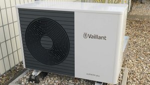 Eine moderne Wärmepumpe von Vaillant steht auf einem Kiesbett, umgeben von einem Zaun und einem gepflegten Garten.