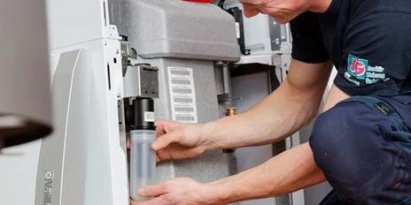 Ein Techniker überprüft sorgfältig eine Heizungsanlage, während er ein transparentes Behältnis in der Hand hält.