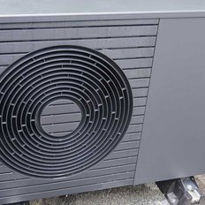 Eine moderne Wärmepumpe in einem Garten, umgeben von grünen Pflanzen und einem Ziegelmauerhintergrund.