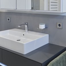 Das stilvolle Waschbecken ist in einem minimalistischen Badezimmer platziert, umgeben von grauen Wänden und einem großen Spiegel.