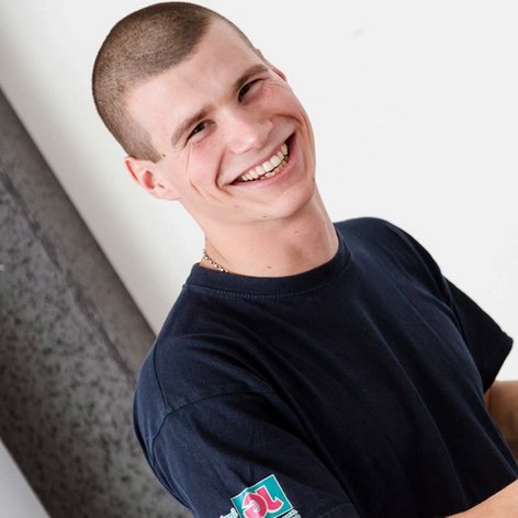 Techniker repariert elektrische Geräte mit Freude und Präzision Ein junger Techniker lächelt, während er mit einem Multimeter an einem elektrischen Gerät arbeitet, um Fehler zu diagnostizieren.