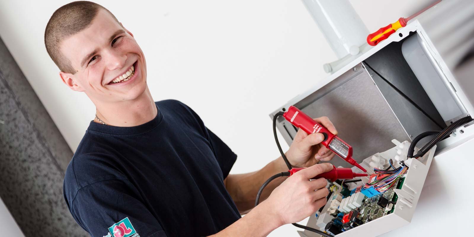 Ein junger Techniker lächelt, während er mit einem Multimeter an einem elektrischen Gerät arbeitet, um Fehler zu diagnostizieren.