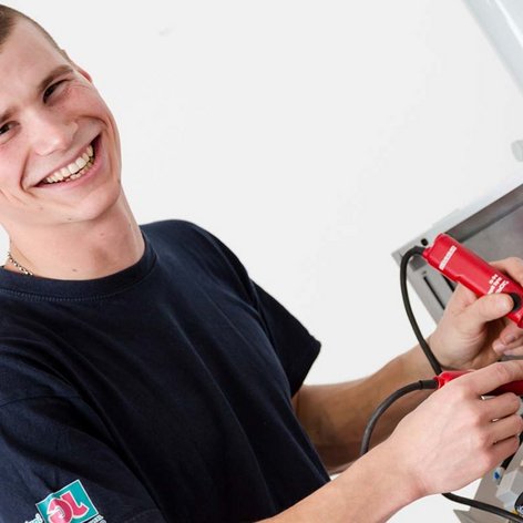 Ein junger Techniker lächelt, während er mit einem Multimeter an einem elektrischen Gerät arbeitet, um Fehler zu diagnostizieren.