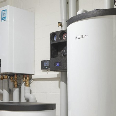 Ein moderner Heizkessel von Vaillant steht an einer weißen Wand, umgeben von Rohren und einem großen Warmwasserspeicher.