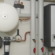Eine moderne Heizungsanlage mit einem großen weißen Speicher und mehreren Rohren, die an der Wand montiert sind.