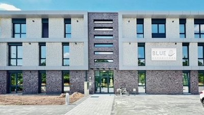 Ein modernes Gebäude mit einer Fassade aus hellen und dunklen Steinen, das den Schriftzug 'BLUE' trägt.