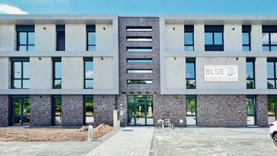 Moderne Architektur des Blue Gebäudes in der Stadt Ein modernes Gebäude mit einer Fassade aus hellen und dunklen Steinen, das den Schriftzug 'BLUE' trägt.