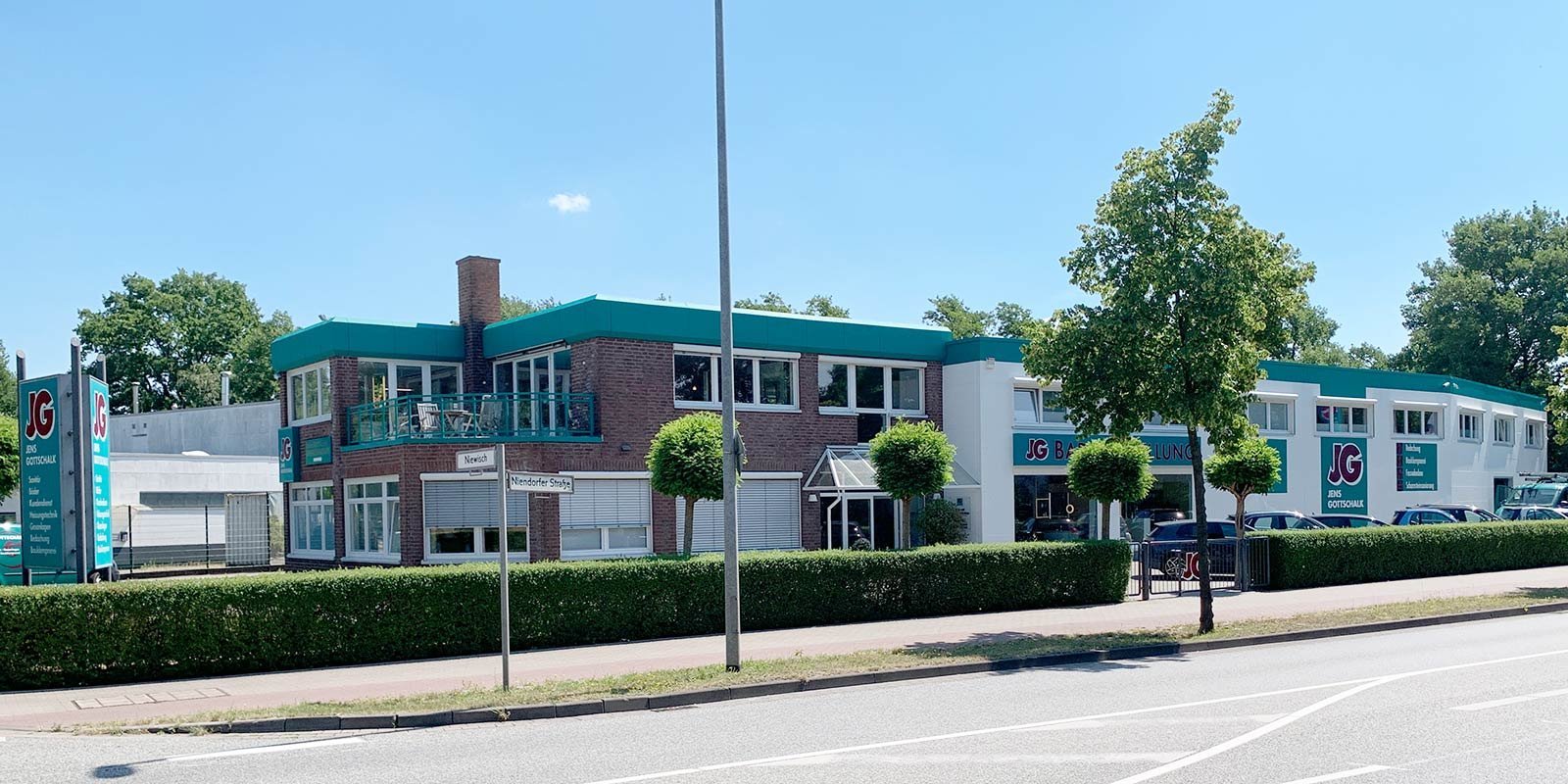 Ein modernes Gebäude mit grünem Dach und großen Fenstern, umgeben von gepflegten Büschen und Bäumen an einer Straße.