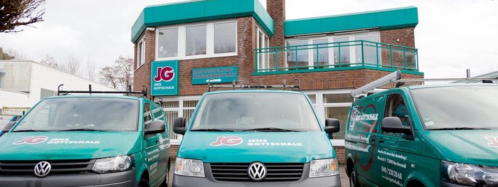 Drei grüne Volkswagen-Fahrzeuge stehen vor einem modernen, zweigeschossigen Gebäude mit einem blauen Dach.