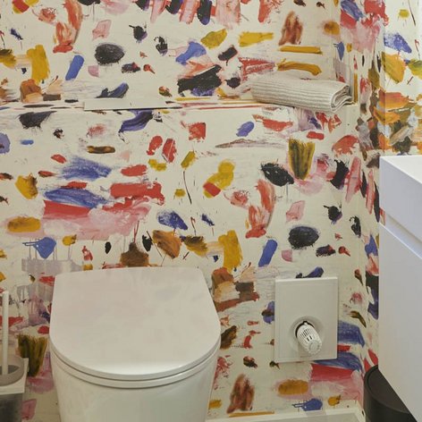 Ein modernes Badezimmer mit einer bunten, künstlerischen Wandgestaltung aus verschiedenen Farbtönen und einem eleganten Waschbecken.