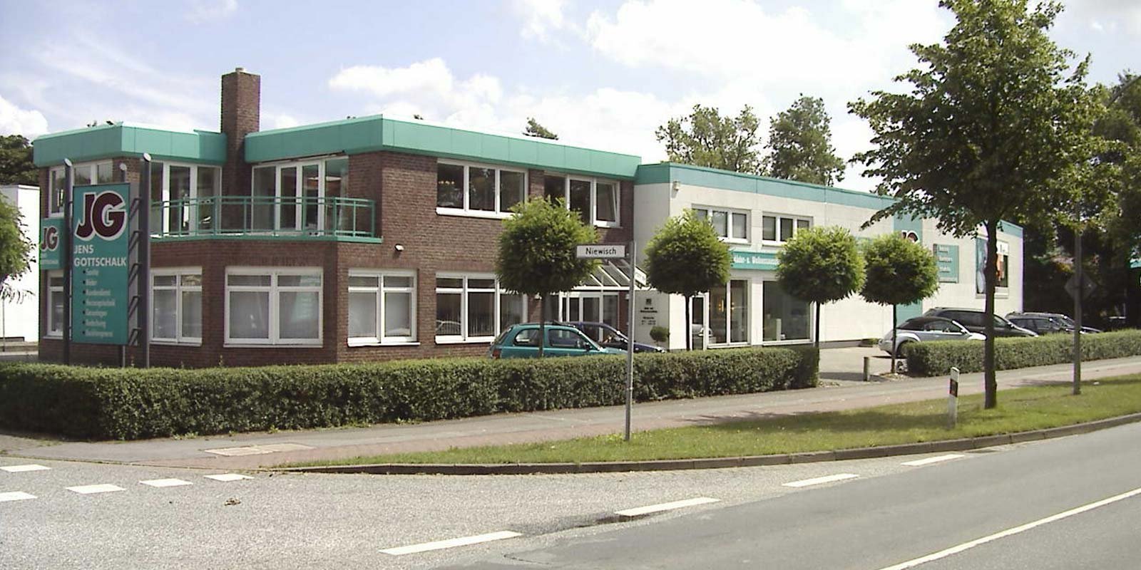 Ein modernes Bürogebäude mit einer auffälligen grünen Dachkante und großen Fenstern, umgeben von gepflegten Büschen.