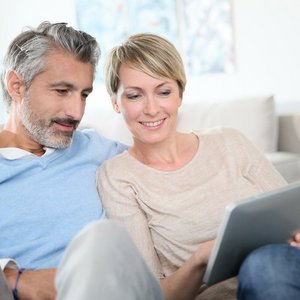 Ein Paaerchen sitzen nebeneinander und schauen auf ein Tablet