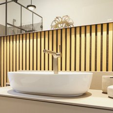 Ein modernes Badezimmer mit einem eleganten, weißen Waschbecken und einem stilvollen Wasserhahn vor einer Holzvertäfelung.