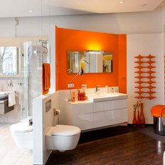 Das Badezimmer bietet eine stilvolle Kombination aus Holz- und Fliesenböden, ergänzt durch orangefarbene Akzente und Pflanzen.