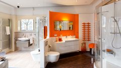 Das Badezimmer bietet eine stilvolle Kombination aus Holz- und Fliesenböden, ergänzt durch orangefarbene Akzente und Pflanzen.