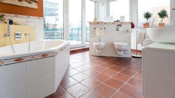 Das Badezimmer zeigt eine stilvolle Badewanne, zwei Toiletten und Pflanzen auf der Fensterbank, die eine frische Atmosphäre schaffen.