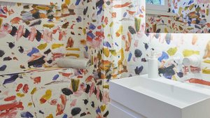 Ein modernes Badezimmer mit einer weißen Waschbeckenanlage vor einer bunten, künstlerisch gestalteten Wand.